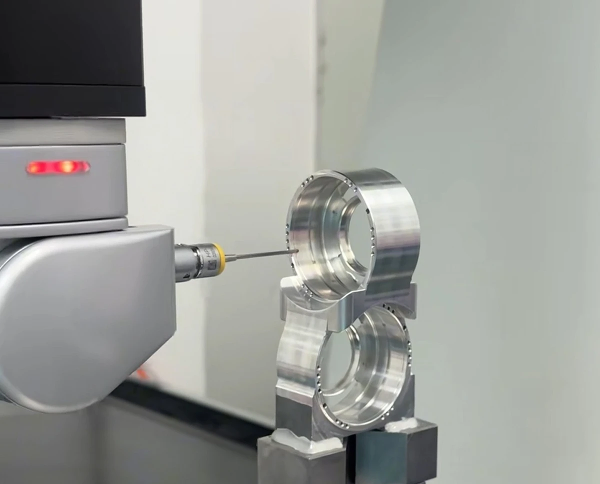 CMM probe measuring a machined metal component with circular bores held in a fixture